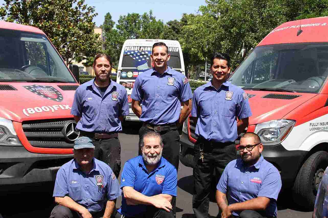 The Patriot Plumbing & Rooter team in branded uniforms in front of the company fleet